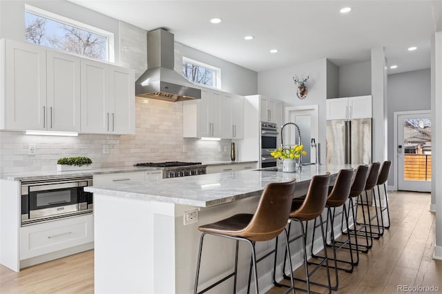 2111 S Franklin St, Denver, CO 80210 - kitchen featuring wall chimney exhaust hood, stainless steel appliances, a center island with sink, light wood-type flooring, and recessed lighting