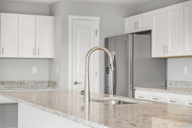 kitchen with light stone countertops, white cabinetry, and stainless steel refrigerator