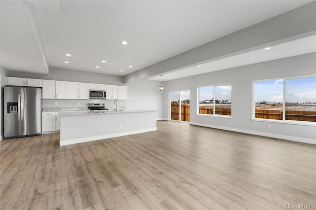 kitchen featuring white cabinets, light wood-type flooring, stainless steel appliances, and hanging light fixtures