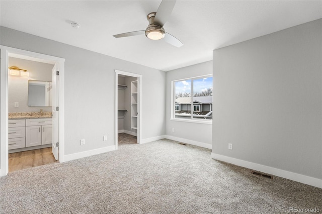 unfurnished bedroom featuring a walk in closet, ceiling fan, ensuite bath, and light carpet