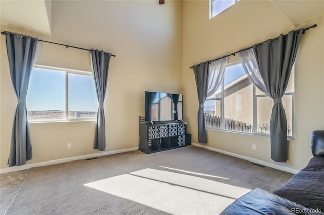 unfurnished living room featuring a high ceiling, a healthy amount of sunlight, and light colored carpet