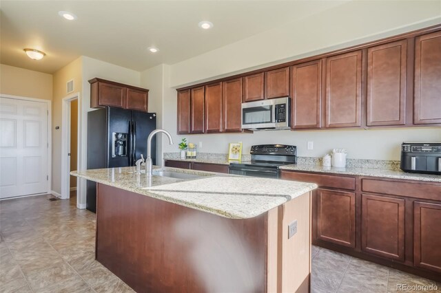 kitchen with sink, black appliances, light stone countertops, and a center island with sink