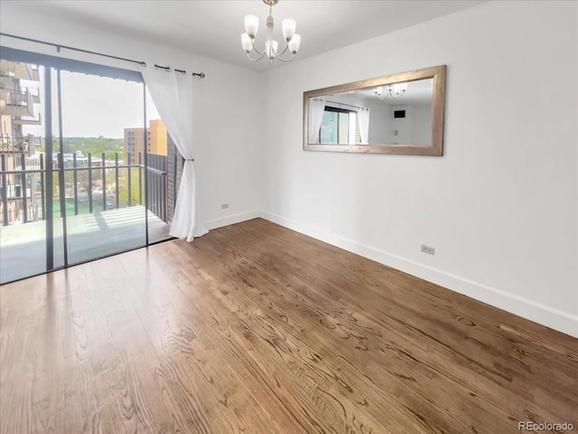 empty room featuring a chandelier, baseboards, and wood finished floors