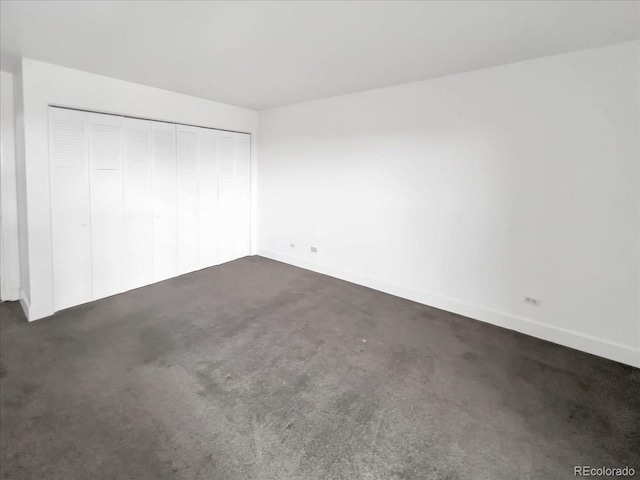 unfurnished bedroom with dark colored carpet, a closet, and baseboards