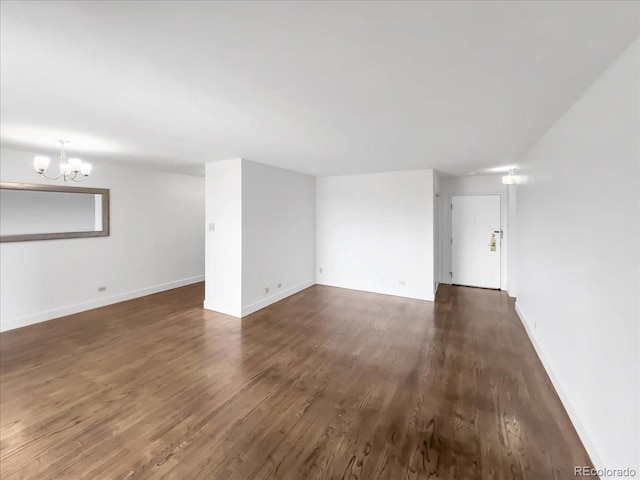 unfurnished living room with dark wood-type flooring, a chandelier, and baseboards