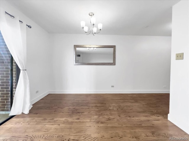 empty room featuring wood finished floors, baseboards, and a chandelier