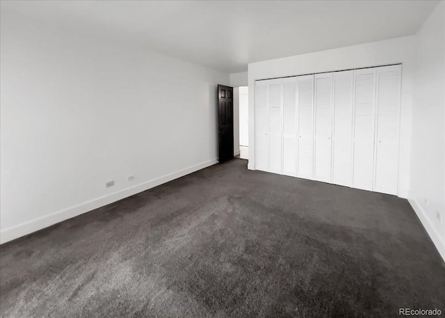unfurnished bedroom with dark carpet, baseboards, and a closet