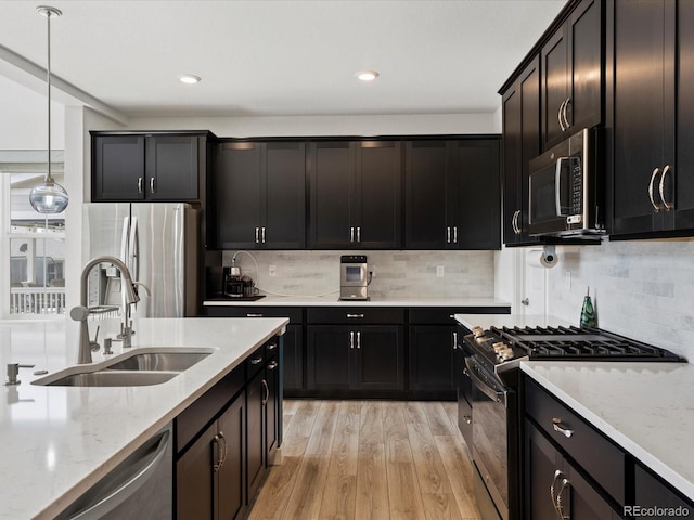 kitchen with pendant lighting, light wood-type flooring, light stone counters, appliances with stainless steel finishes, and a sink