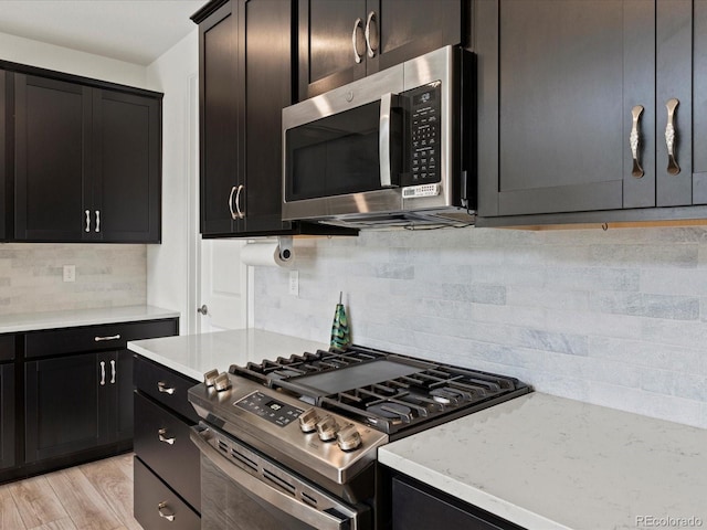 kitchen with light wood-style flooring, tasteful backsplash, appliances with stainless steel finishes, light stone countertops, and dark cabinets