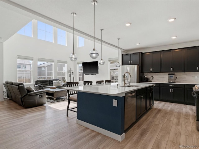 kitchen featuring a sink, stainless steel appliances, light countertops, open floor plan, and light wood-type flooring