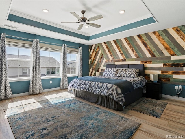 bedroom with a tray ceiling, multiple windows, wood finished floors, and visible vents