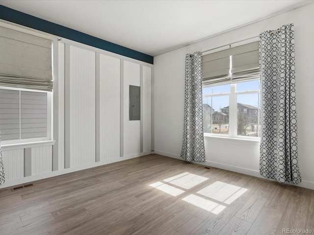 empty room with electric panel, visible vents, baseboards, and wood finished floors