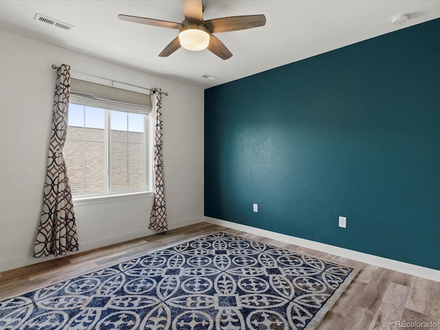 empty room featuring ceiling fan, visible vents, baseboards, and wood finished floors