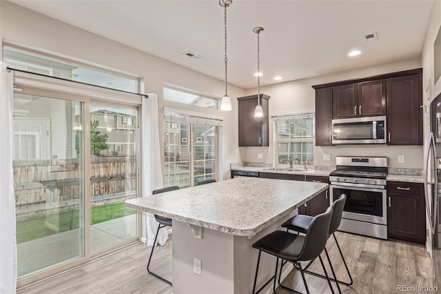 18112 E 104th Way, Commerce City, CO 80022 - kitchen with appliances with stainless steel finishes, a sink, light wood-style flooring, a breakfast bar area, and dark brown cabinetry