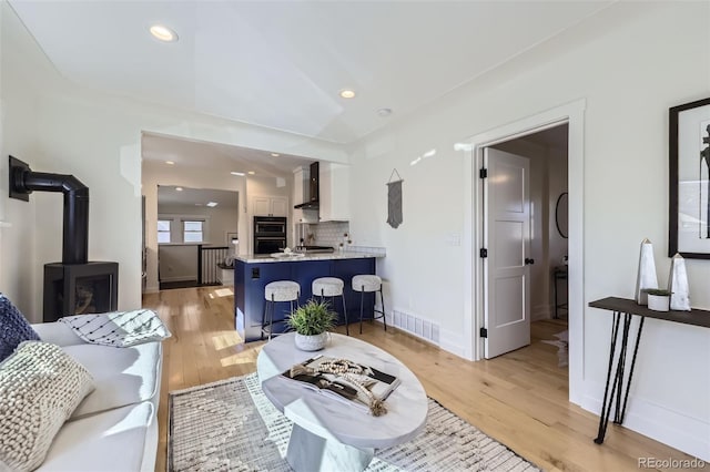 living area featuring a wood stove, light wood finished floors, visible vents, and recessed lighting