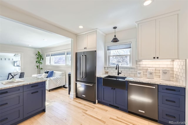 kitchen with tasteful backsplash, high end refrigerator, light wood-style flooring, stainless steel dishwasher, and a sink