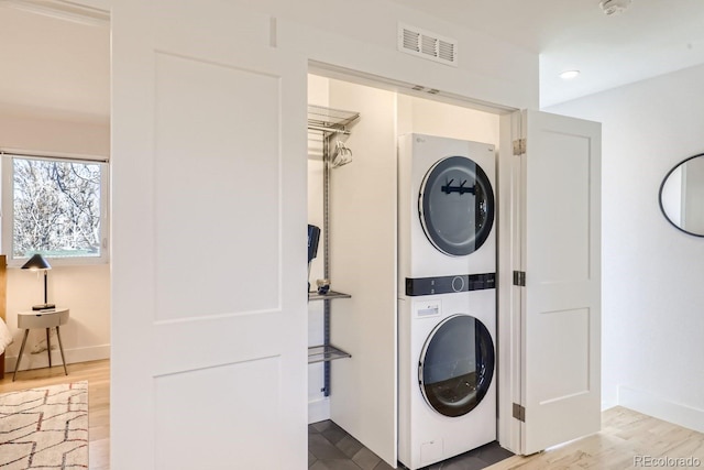 laundry room featuring laundry area, stacked washer and dryer, wood finished floors, visible vents, and baseboards