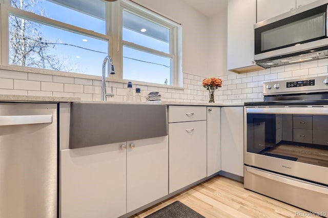 kitchen featuring decorative backsplash, stainless steel appliances, light wood-type flooring, white cabinetry, and a sink