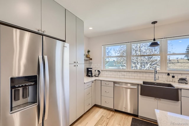 kitchen featuring pendant lighting, stainless steel appliances, tasteful backsplash, light wood-style flooring, and a sink