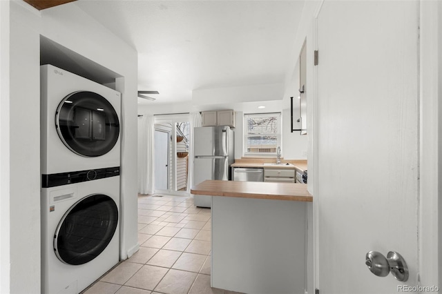 laundry room featuring sink, light tile patterned floors, and stacked washing maching and dryer