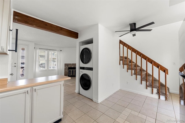 clothes washing area featuring ceiling fan, light tile patterned flooring, a fireplace, and stacked washer and clothes dryer