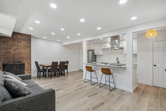 7995 E Mississippi Ave Unit A4, Denver, CO 80247 - kitchen with wall chimney range hood, a breakfast bar area, white cabinets, light wood-type flooring, and recessed lighting