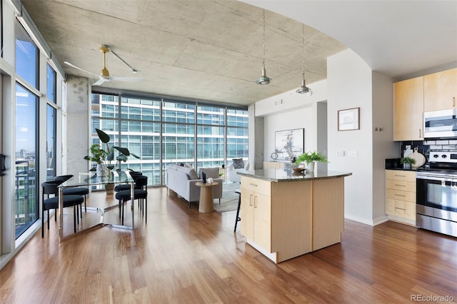 kitchen with stainless steel appliances, expansive windows, dark stone counters, and hardwood / wood-style flooring