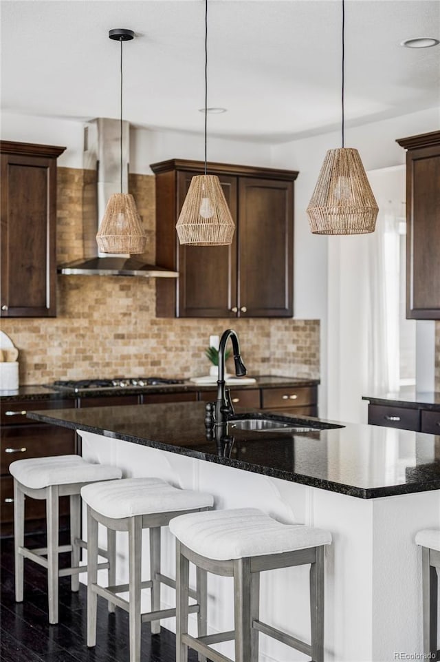 kitchen featuring hanging light fixtures, backsplash, dark stone counters, and wall chimney exhaust hood