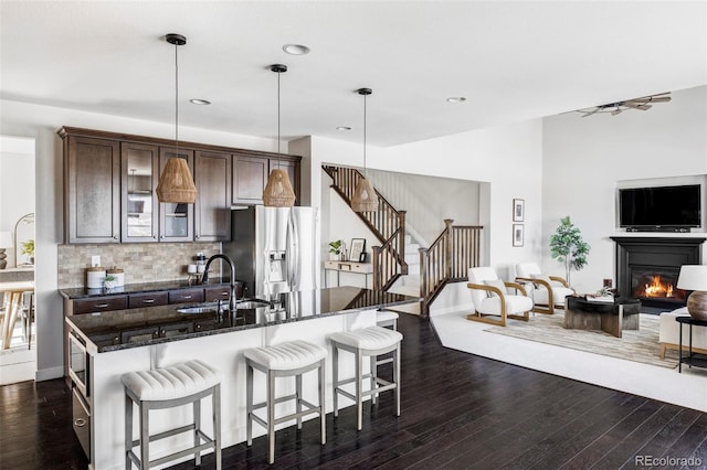 kitchen with pendant lighting, sink, backsplash, dark brown cabinetry, and stainless steel refrigerator with ice dispenser