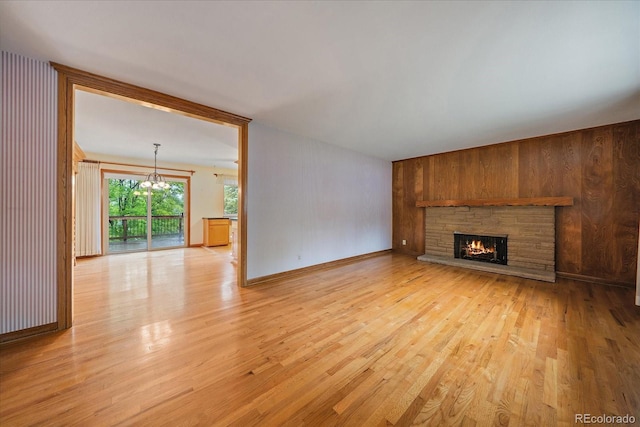 7077 Dudley Dr, Arvada, CO 80004 - unfurnished living room with light wood-style floors, a chandelier, a stone fireplace, and wood walls