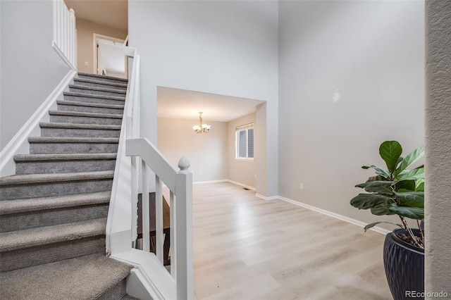 staircase with wood-type flooring, a high ceiling, and an inviting chandelier