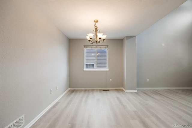 empty room featuring light wood-type flooring and a notable chandelier