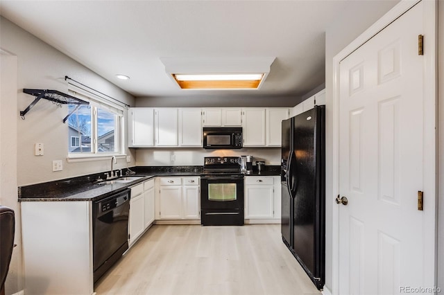 kitchen with sink, dark stone countertops, light hardwood / wood-style floors, white cabinets, and black appliances