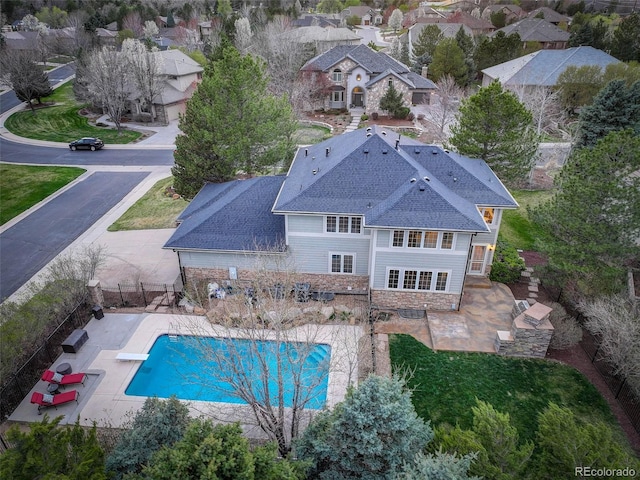 exterior space with a shingled roof, stone siding, an outdoor pool, a fenced backyard, and a patio area