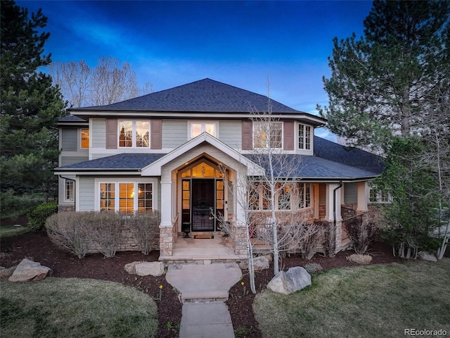 view of front of home with a front lawn, roof with shingles, and stone siding