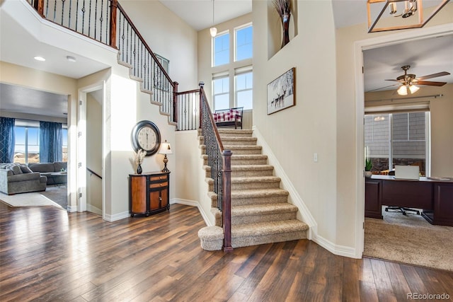 stairs featuring a ceiling fan, a high ceiling, baseboards, and hardwood / wood-style floors