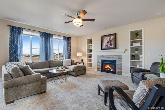 living room featuring baseboards, built in features, carpet flooring, a fireplace, and a ceiling fan