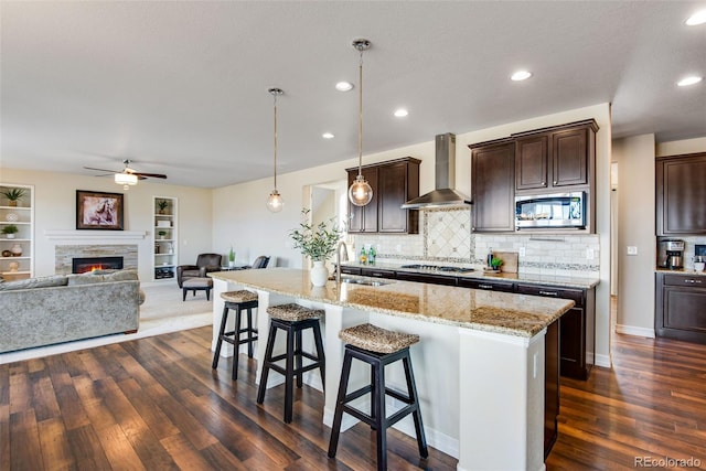 kitchen featuring wall chimney range hood, a kitchen breakfast bar, a fireplace, stainless steel appliances, and a sink