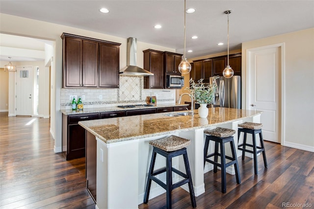 kitchen featuring dark wood-style flooring, a sink, stainless steel appliances, wall chimney exhaust hood, and tasteful backsplash