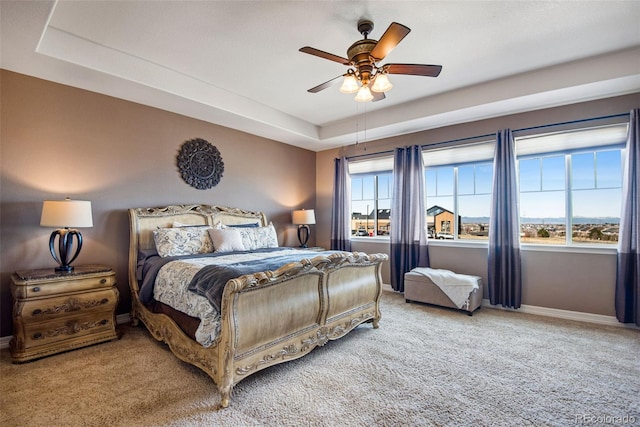 carpeted bedroom featuring a raised ceiling, a ceiling fan, and baseboards