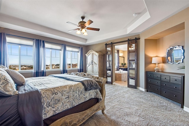 carpeted bedroom featuring a ceiling fan, baseboards, ensuite bath, a barn door, and a raised ceiling