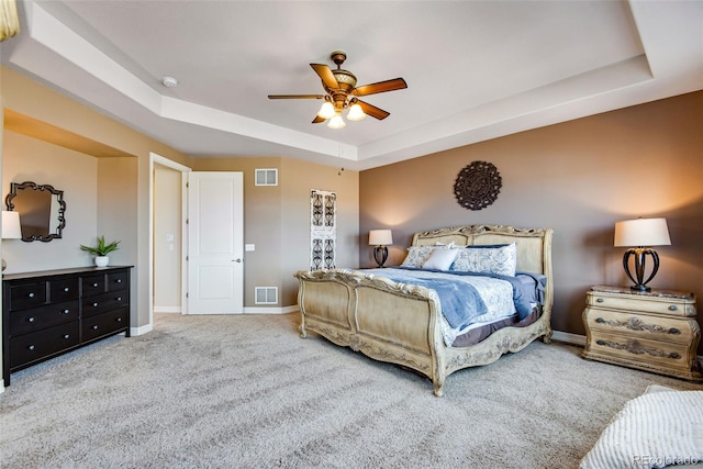 carpeted bedroom featuring visible vents, a raised ceiling, baseboards, and a ceiling fan