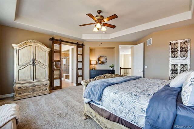 bedroom with a tray ceiling, a barn door, visible vents, and light carpet