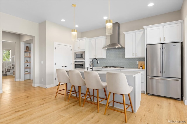 13729 Vallejo Loop, Broomfield, CO 80023 - kitchen featuring appliances with stainless steel finishes, wall chimney range hood, light wood finished floors, light countertops, and an island with sink
