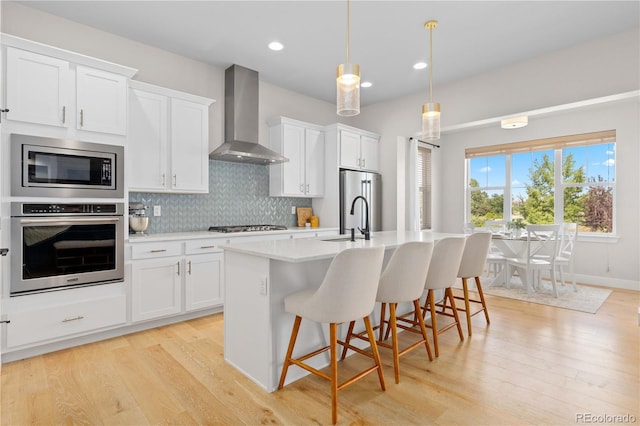 13729 Vallejo Loop, Broomfield, CO 80023 - kitchen featuring appliances with stainless steel finishes, wall chimney exhaust hood, a center island with sink, light countertops, and light wood-style flooring