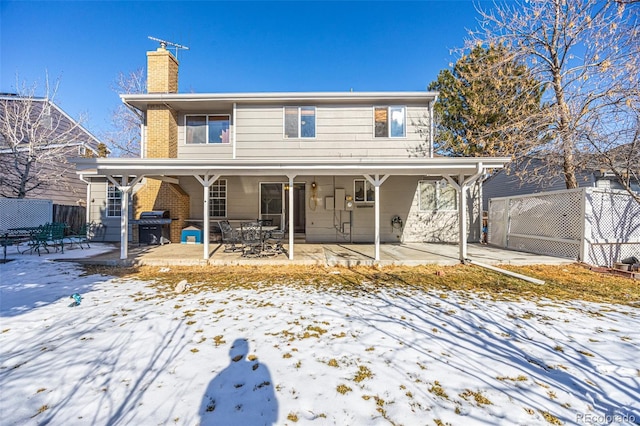 snow covered back of property featuring a patio