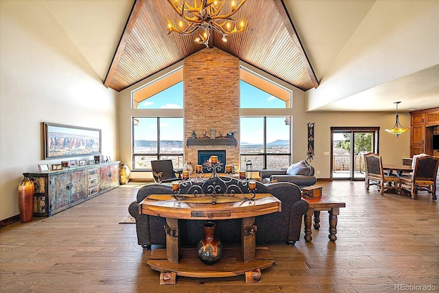 living area with baseboards, an inviting chandelier, hardwood / wood-style floors, a stone fireplace, and high vaulted ceiling