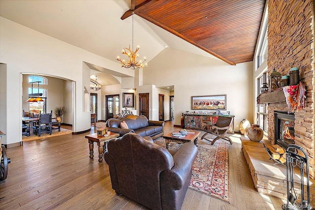 living area with arched walkways, an inviting chandelier, high vaulted ceiling, hardwood / wood-style floors, and a fireplace