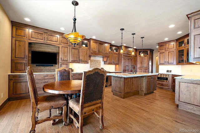 kitchen featuring hardwood / wood-style flooring, brown cabinets, an island with sink, glass insert cabinets, and recessed lighting