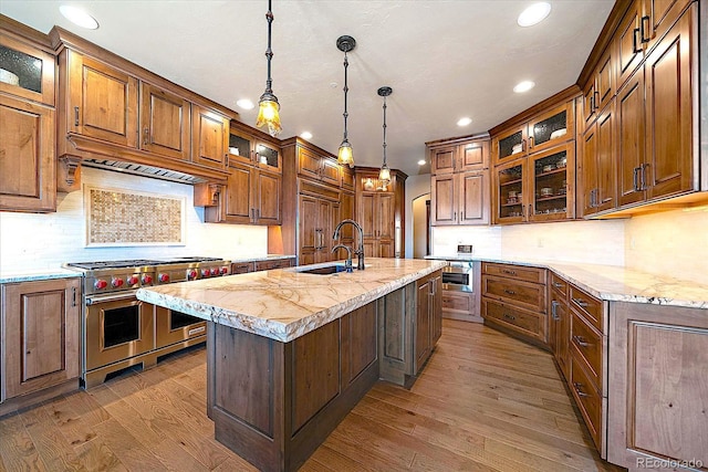 kitchen with recessed lighting, backsplash, wood finished floors, a center island with sink, and double oven range